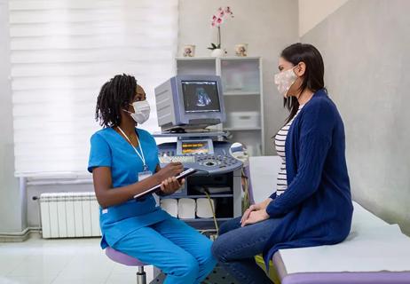 Healthcare worker taking notes while talking to a woman in an exam room