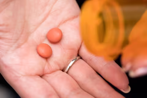 Palm of hand with two pills poured onto it from medication bottle
