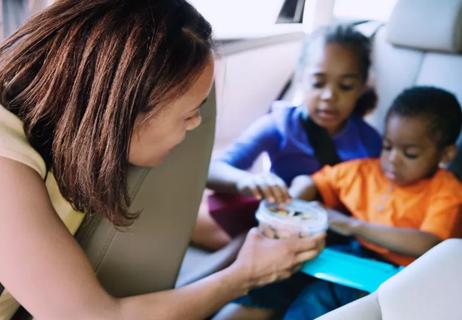 Parent sharing bowl of nuts with children while on road trip.