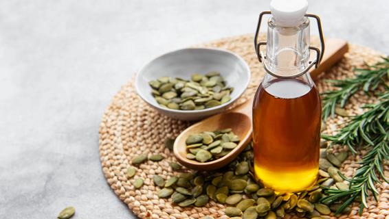 Bottle of pumpkin seed oil on mat with pumpkin seeds and sprigs