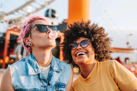 Two people wearing sunglasses, laughing and bubble gum blowing