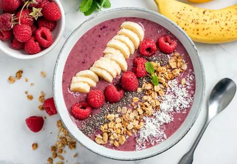 An acai smoothie bowl topped with banana, raspberries, coconut and oats.