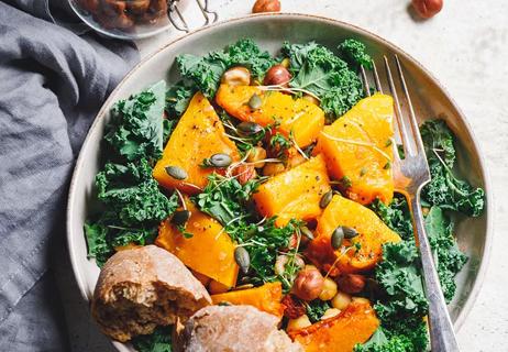 Grilled butternush squash on a white plate with kale and nuts sprinkled on top.