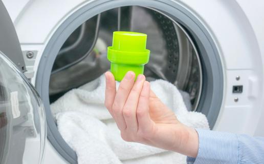 Hand holding laundry detergent cap in front of open dryer with towels in it