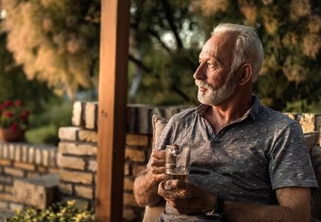 Older man deep in thought on porch at early evening