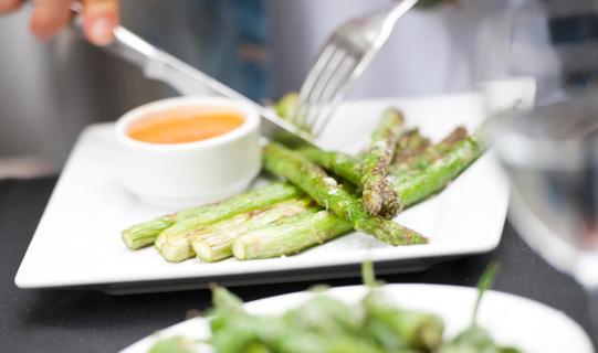 Hands with fork and knife cutting grilled asparagus