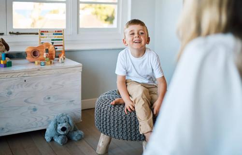 Happy child sitting on stool in healthcare office, with toys around