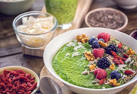 A table with a bowel of green food and berries