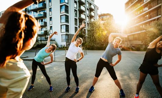 Group of people outside in city, doing over-shoulder stretching