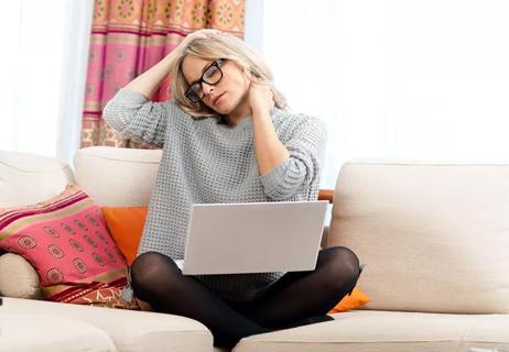 woman with headache while workingon laptop from couch