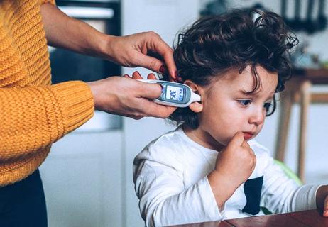 Person taking temperature of child using ear thermometer.