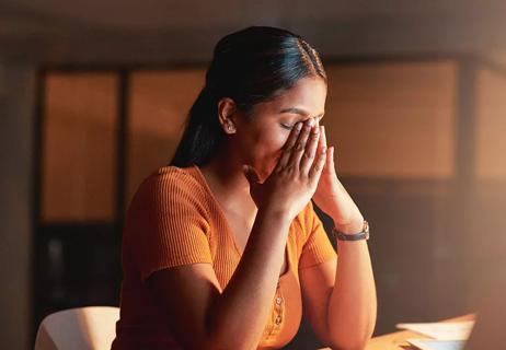 Person stressed with hands over their face in darkened room.