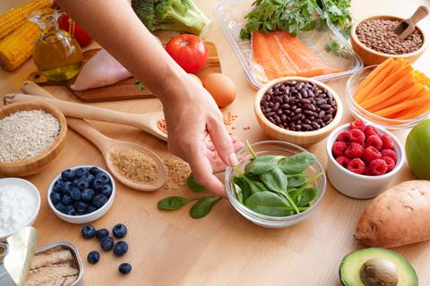 Hand picking up bowl of fresh spinach, with other healthy, fresh foods all around table