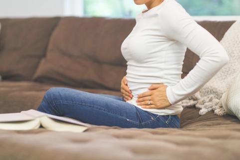 Woman sitting on sofa, holding pelvic area in pain