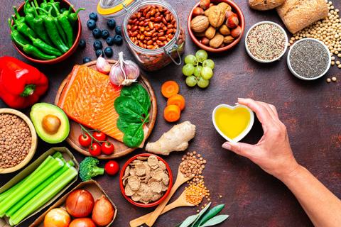 Heart-healthy foods, including salmon, nuts, greens and fruits, and oil in a heart shaped dish