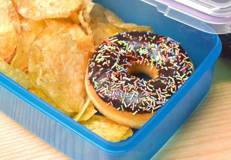 Closeup of a lunch box with potato chips and a donut, food with transfat content.