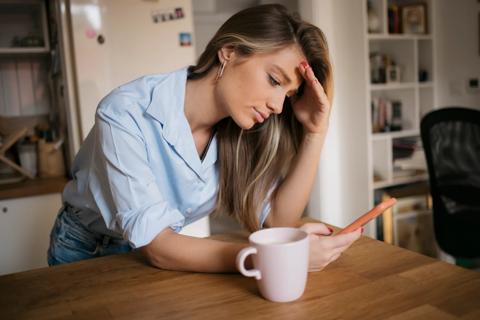 Woman leaning on counter with hand against forehead, looking at phone