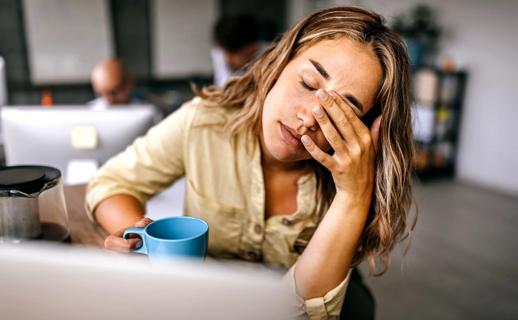 Tired woman, hand on closed eyes, holding cup of coffee