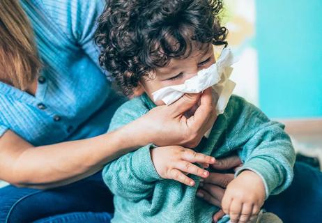 While sitting on floor, parent wipes toddler's nose with tissue.