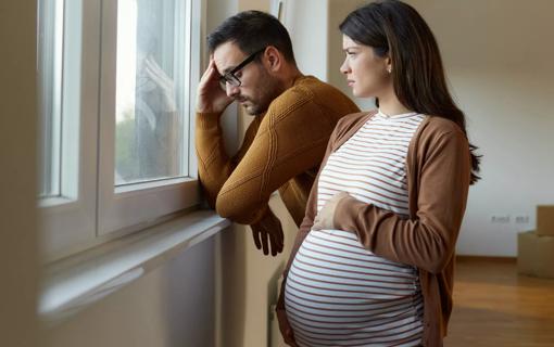 Male and pregnant female looking out window pensively