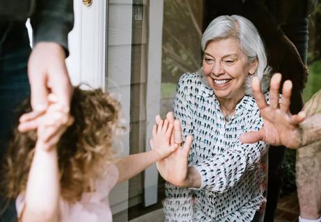 older person and child touch hands through a glass door while smiling