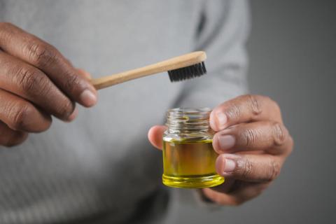 Person holding black-bristle toothbrush and jar or oil