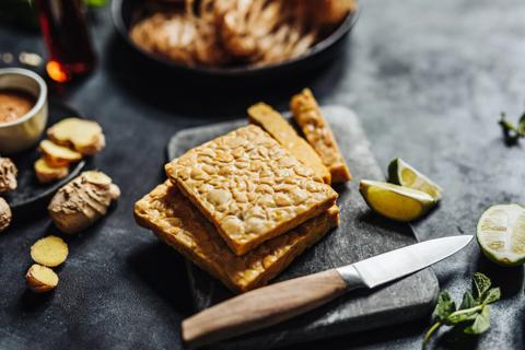 Two cakes of tempeh on black cutting board, with lime and knife