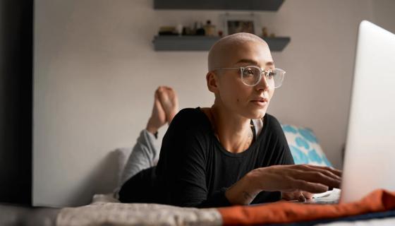 Woman with shorn hair lying on bed looking at laptop