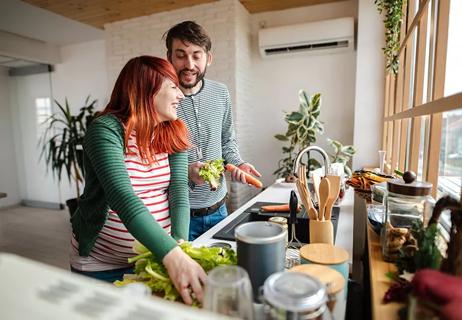 Two people talking and laughing while preparing lettuce and carrots, with one person pregnant.