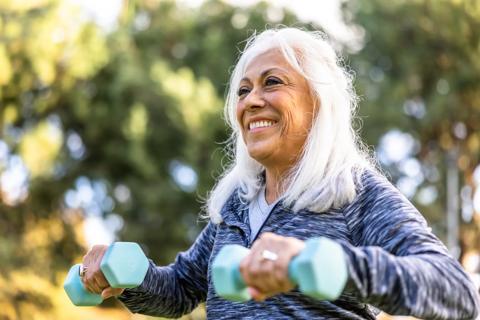 Smiling older woman outside lifting five-pound weights