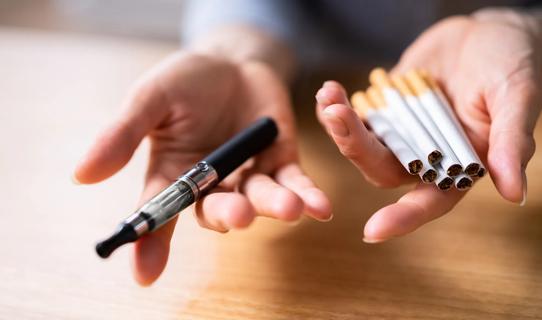 Two hands, one holding a vape, the other, cigarettes