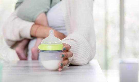 Caregiver holding baby and picking up bottle of milk