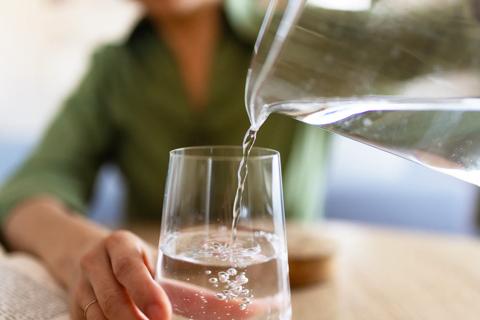 Person pouring a glass of water from a glass pitcher