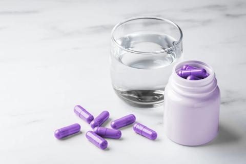 Glass of water on table, with medicine bottle of purple capsules, and capsules on table