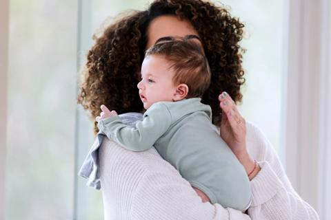 Caregiver burping baby, holding baby over their shoulder, patting baby's back