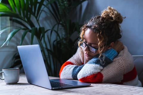Person leaning on elbows with eyes closed at their laptop