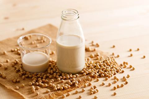 Bottle and glass of soy milk, with soy beans scattered on table