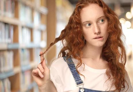 Worried person twists ends of hair while in school library.
