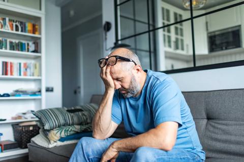 Person sitting on couch, eye glasses pushed up on head, head in hand, eyes closed