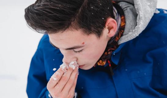 Boy holding nostril from a nosebleed outside in the snow