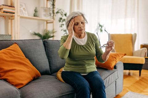 Older woman sitting on couch, with hand to head, feeling dizzy