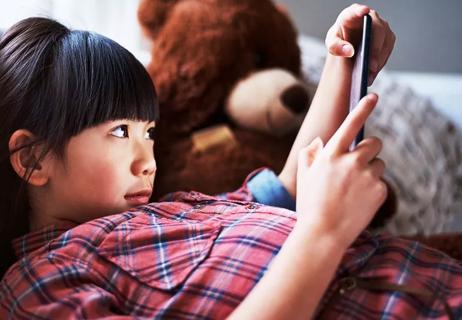 Young girl lying on couch playing on a digital tablet