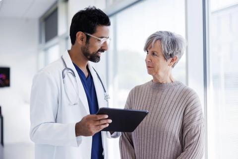 Healthcare provider holding a tablet, talking to patient in medical setting