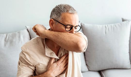 Person coughing into their elbow, with hand on their chest