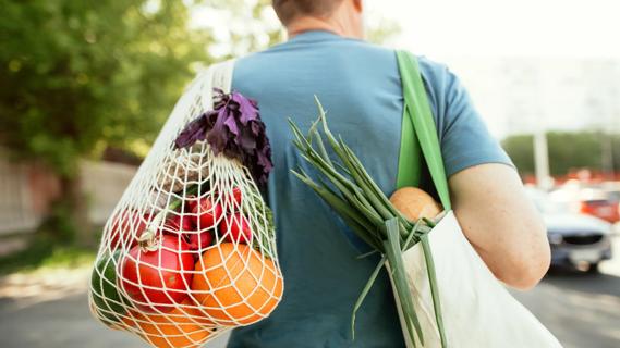Person walking with net of fresh fruits and veggies and bag of fresh foods