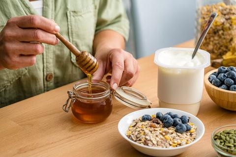 Person getting honey from a jar to put in bowl of oats, fruit and yogurt