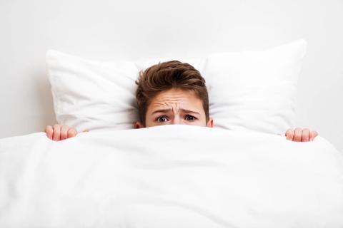 Teenager in bed with covers pulled up to their eyes, looking worried