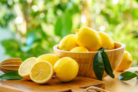 A wooden bowl of whole lemons, with cut lemons around it, on an outdoor table