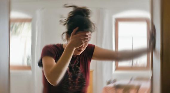 Person with hand on forehead, leaning on doorway jamb, room spinning