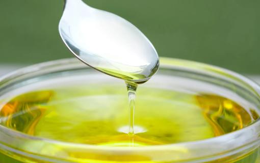 Spoonful of oil dripping into a jar of oil